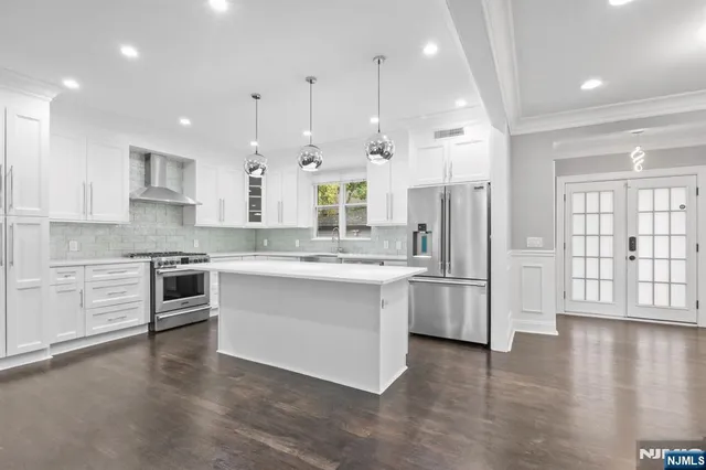 a large kitchen with stainless steel appliances kitchen island granite countertop a stove a sink a refrigerator and white cabinets with wooden floor