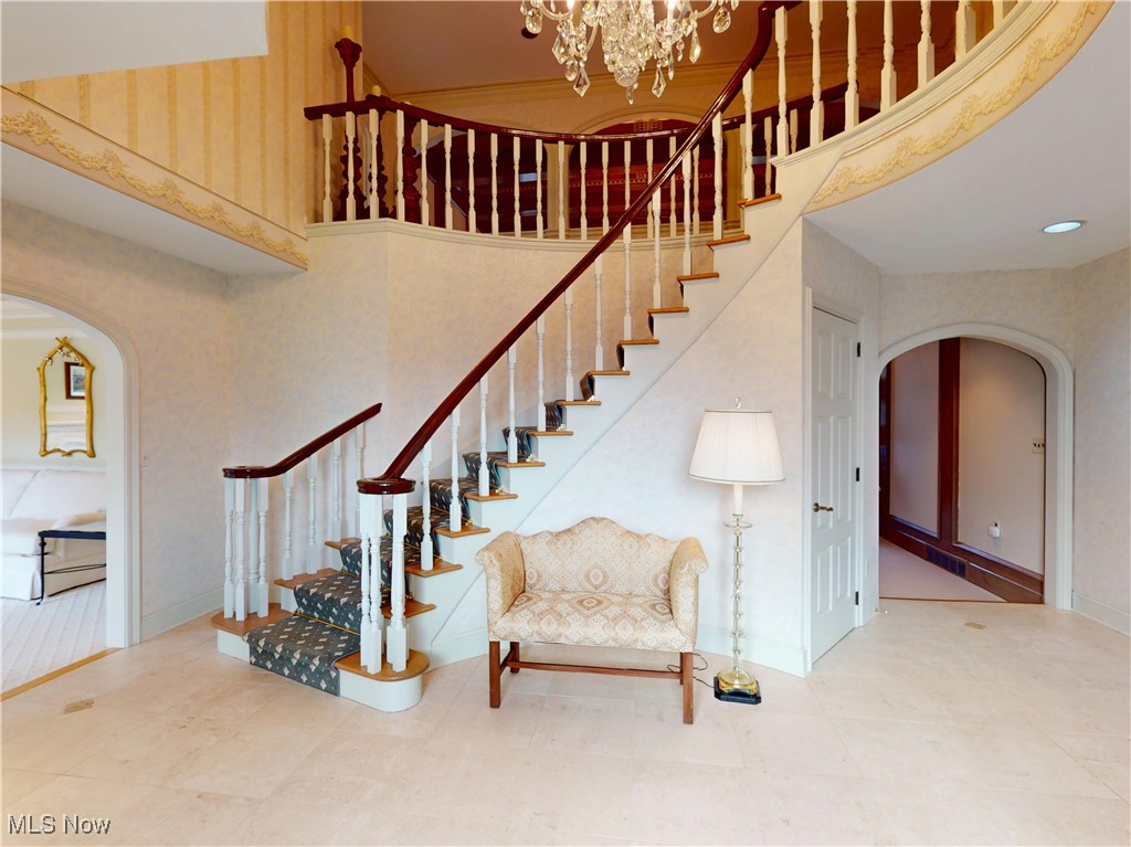 9870 Hobart Road Willoughby, OH 44094 - Photo 4 of 50 Stairway with baseboards, arched walkways, a high ceiling, and a notable chandelier