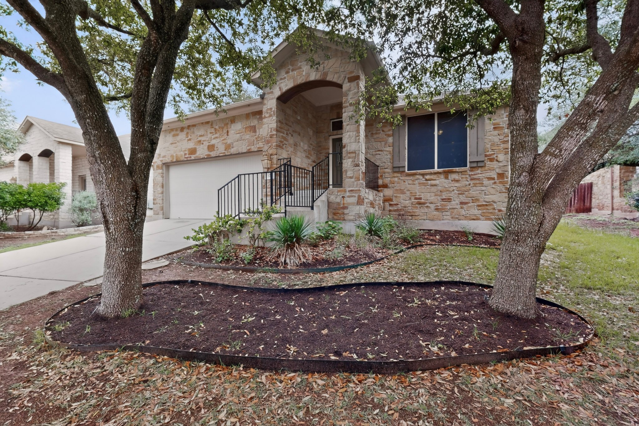 178 Limestone Trail Austin, TX 78737 - Photo 3 of 40 Stone facade residence featuring a covered entry porch with black metal railings, an integrated two-car garage, and established front yard trees