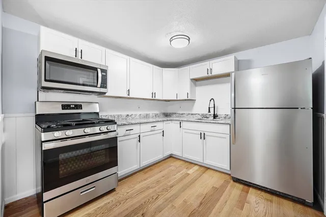a kitchen with white cabinets stainless steel appliances and wooden floor