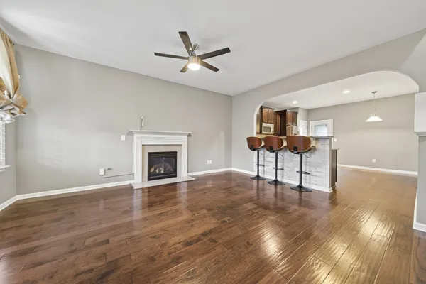a view of a livingroom with a fireplace a ceiling fan and a kitchen view