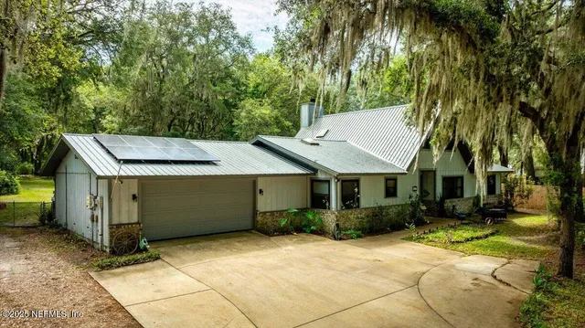 a view of a white house next to a yard with plants and large trees