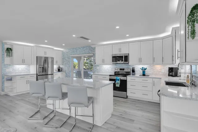 a kitchen with stainless steel appliances kitchen island granite countertop a stove a sink a refrigerator and white cabinets with wooden floor