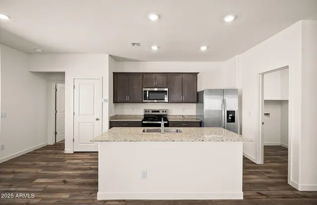 a kitchen with stainless steel appliances granite countertop a stove a refrigerator a sink a microwave and white cabinets with wooden floor