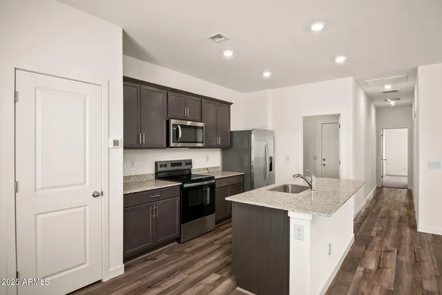 a kitchen with stainless steel appliances granite countertop a refrigerator a sink dishwasher a stove and white countertops with wooden floor