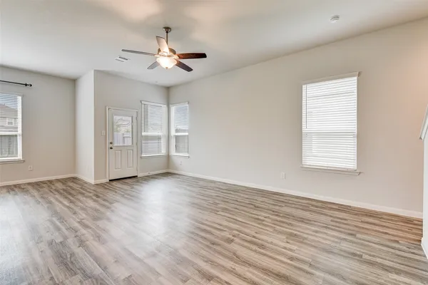 an empty room with wooden floor chandelier fan and windows