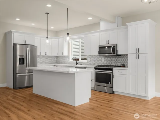 a kitchen with stainless steel appliances granite countertop a refrigerator a stove a sink and white cabinets with wooden floor