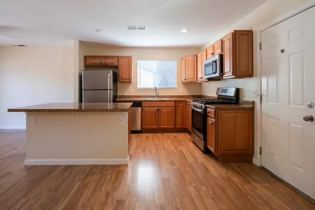 a kitchen with stainless steel appliances granite countertop a stove top oven a sink dishwasher and a refrigerator with wooden floor