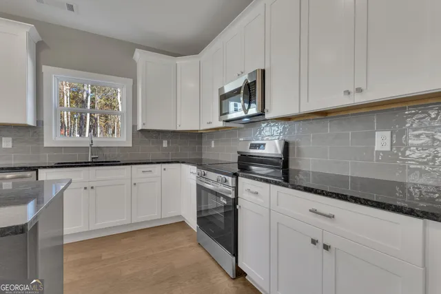 a kitchen with stainless steel appliances granite countertop a stove top oven a sink and white cabinets