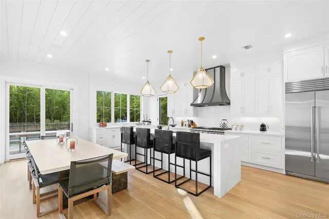 a kitchen with stainless steel appliances granite countertop a stove a refrigerator a kitchen island a dining table and chairs with wooden floor