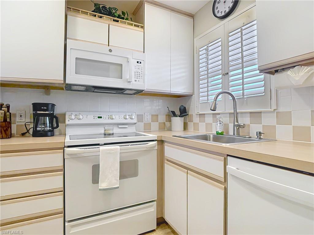 150 Turtle Lake Court, Unit 309 Naples, FL 34105 - Photo 11 of 42 Kitchen featuring white appliances, a sink, tasteful backsplash, light countertops, and white cabinets