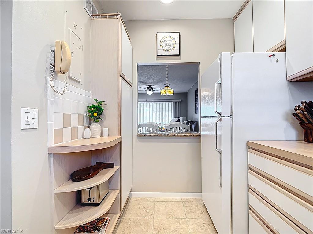 150 Turtle Lake Court, Unit 309 Naples, FL 34105 - Photo 12 of 42 Kitchen with freestanding refrigerator, white cabinets, open shelves, backsplash, and light countertops