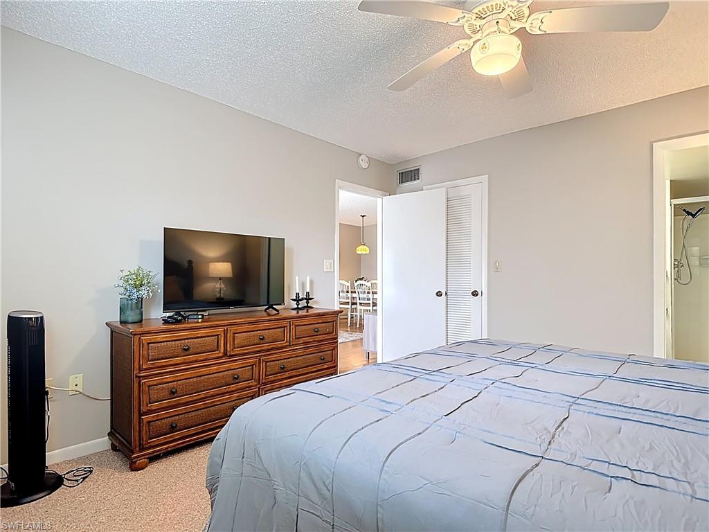 150 Turtle Lake Court, Unit 309 Naples, FL 34105 - Photo 23 of 42 Bedroom with light colored carpet, baseboards, a textured ceiling, a ceiling fan, and a closet