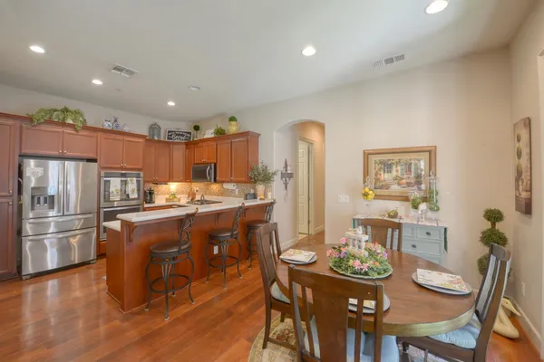 a kitchen with stainless steel appliances granite countertop a refrigerator a stove a sink a dining table and chairs