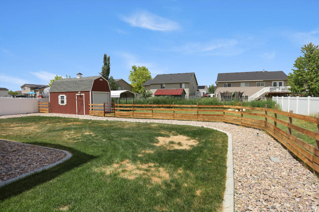 3636 West 910 South Syracuse, UT 84075 - Photo 64 of 70 Spacious backyard featuring a red barn-style shed with a gambrel roof, a gravel pathway, a light wood three-rail fence, and a white privacy fence