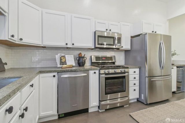 a kitchen with stainless steel appliances granite countertop white cabinets a refrigerator a sink and a stove