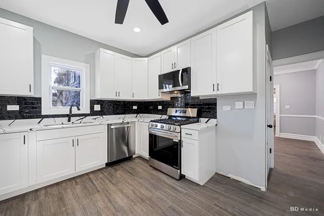 a kitchen with stainless steel appliances granite countertop a stove top oven a sink and white cabinets with wooden floor