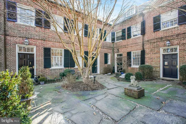 a view of a brick house with many windows plants and large tree