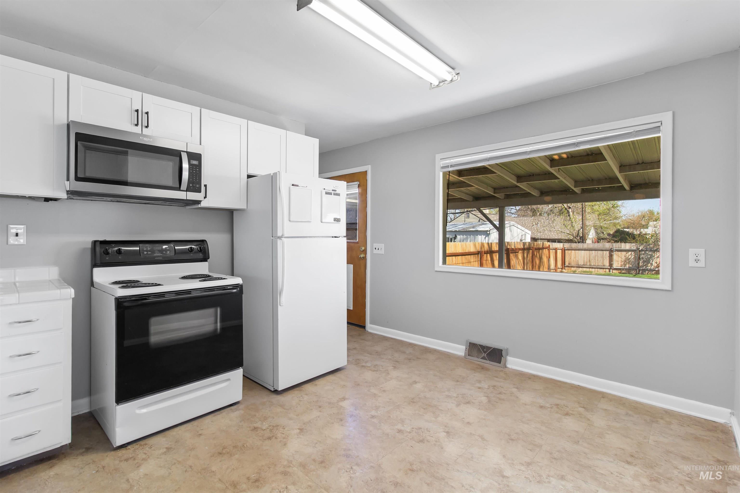 412 Madison Street Twin Falls, ID 83301 - Photo 5 of 42 Kitchen with electric stove, stainless steel microwave, freestanding refrigerator, white cabinetry, and tile countertops