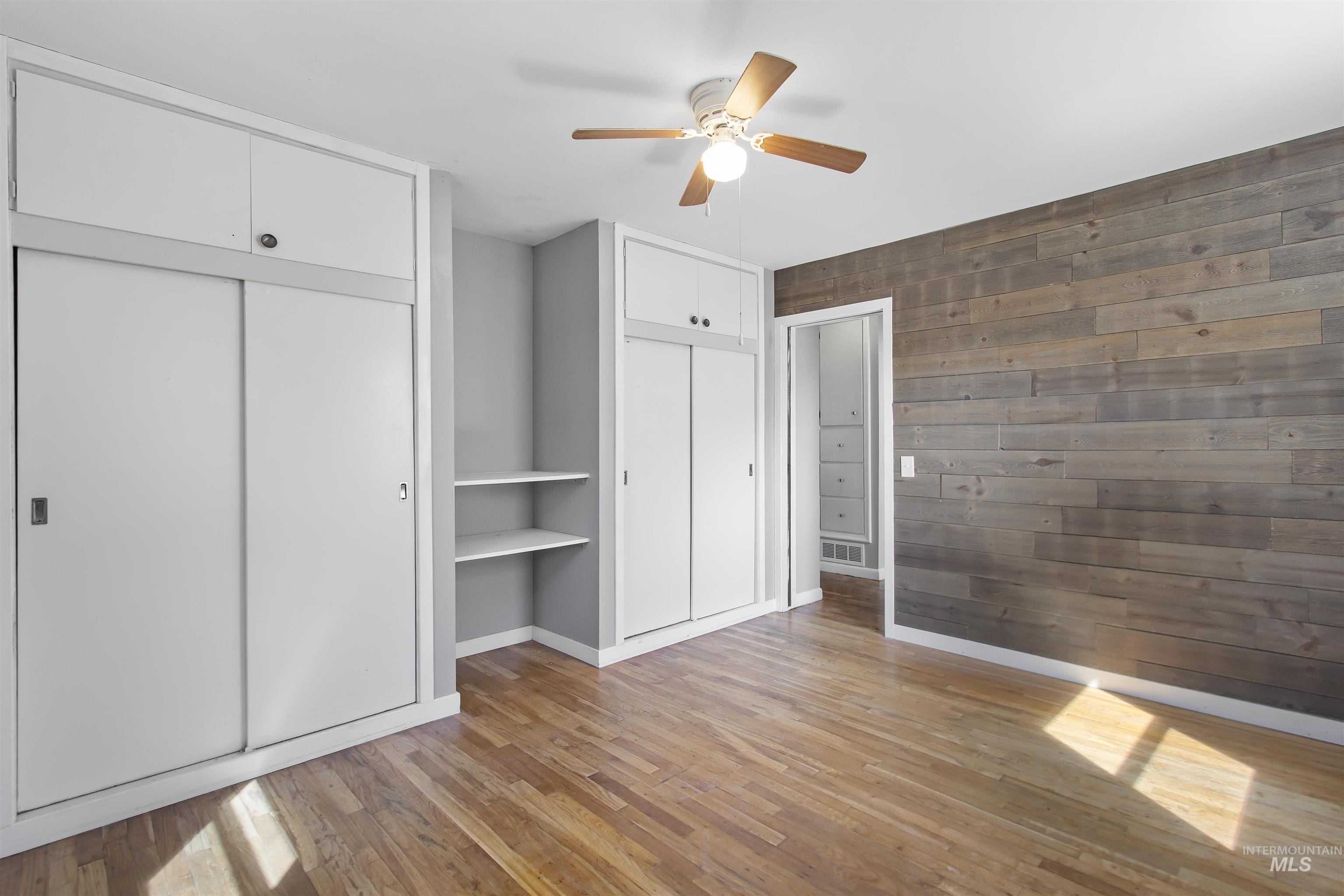 412 Madison Street Twin Falls, ID 83301 - Photo 8 of 42 Unfurnished bedroom with wood walls, two closets, light wood-style flooring, and a ceiling fan