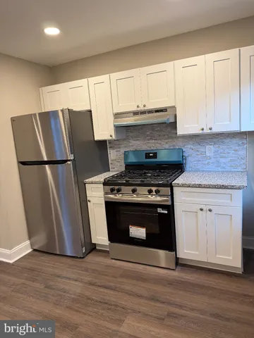 a kitchen with granite countertop a refrigerator stove and white cabinets