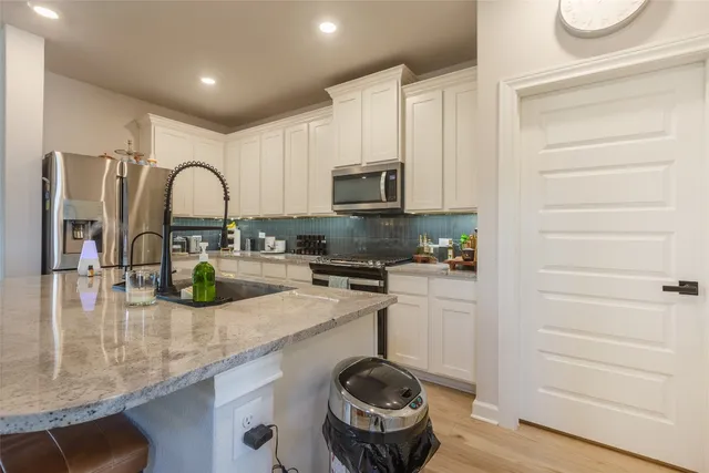 a kitchen with stainless steel appliances granite countertop a refrigerator oven a sink a stove and white cabinets with wooden floor