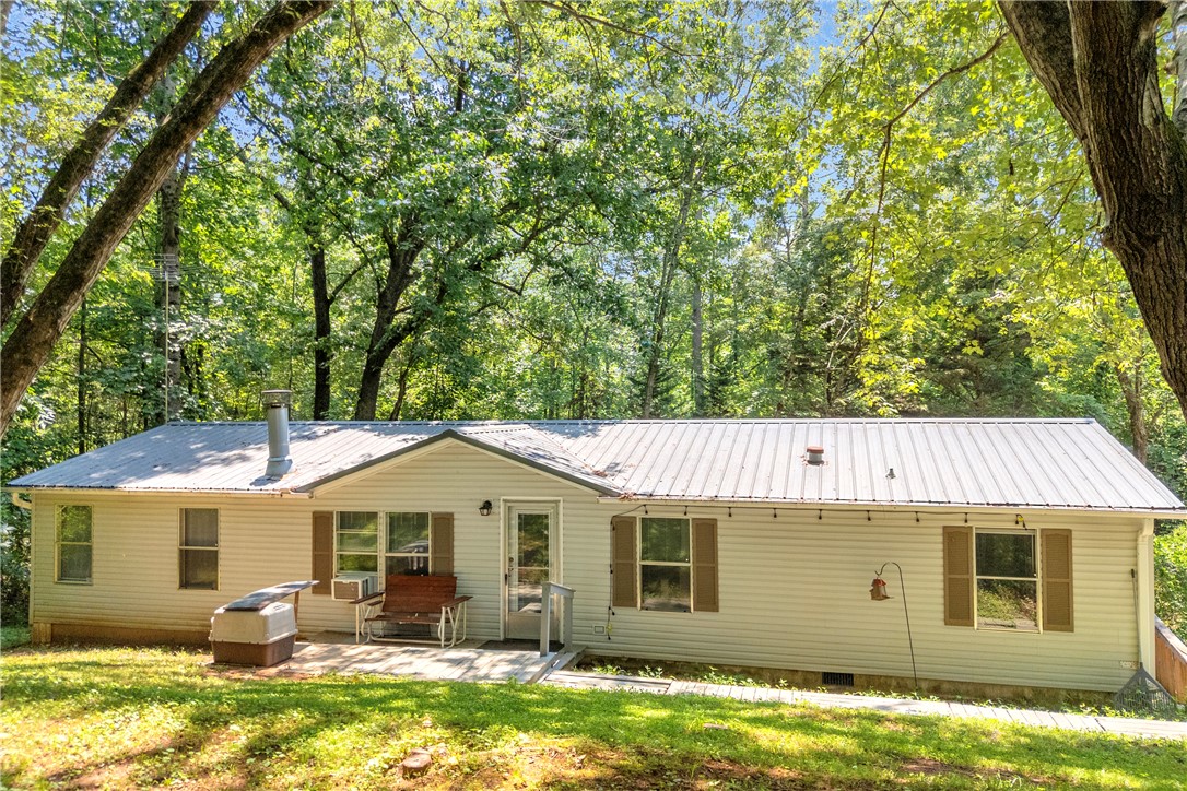 A quaint residence nestled amidst verdant woods, featuring a durable metal roof and a welcoming front patio.