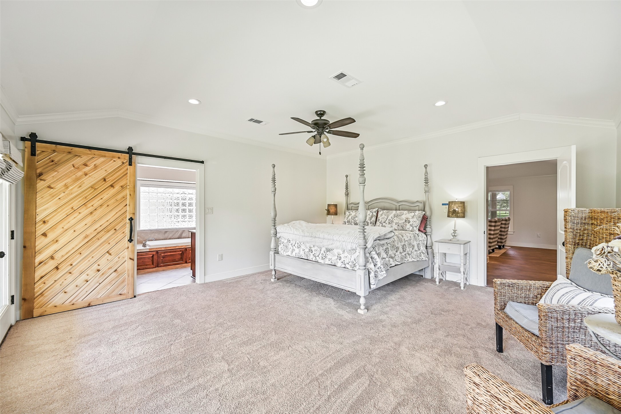 3042 Poskey Road Anahuac, TX 77514 - Photo 34 of 50 Spacious bedroom with large windows showcasing scenic greenery. Features a cozy bed, wicker chairs, ceiling fan, and a sliding barn door to an ensuite bathroom. Bright and inviting!