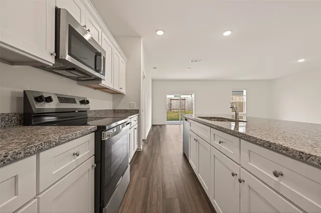 a kitchen with granite countertop cabinets stainless steel appliances a sink and wooden floor