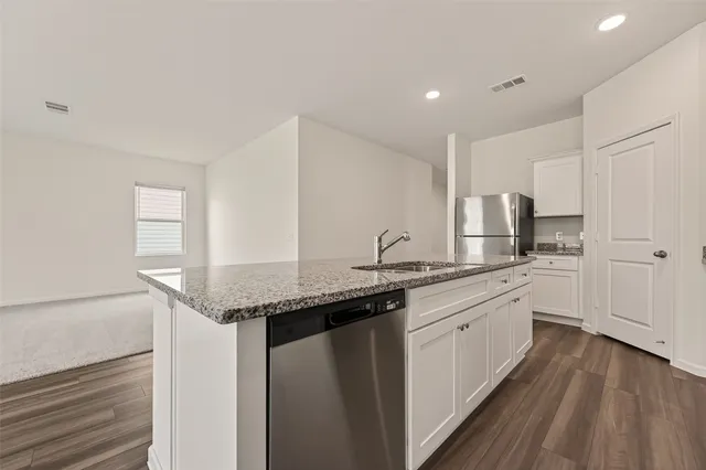 a kitchen with stainless steel appliances granite countertop a refrigerator a stove a sink and white cabinets with wooden floor