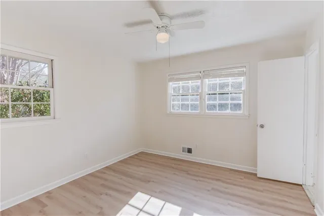 an empty room with wooden floor ceiling fan and windows