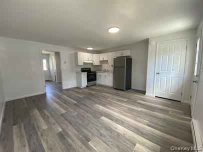 Kitchen featuring white cabinets, appliances with stainless steel finishes, dark wood-style floors, baseboard heating, and light countertops