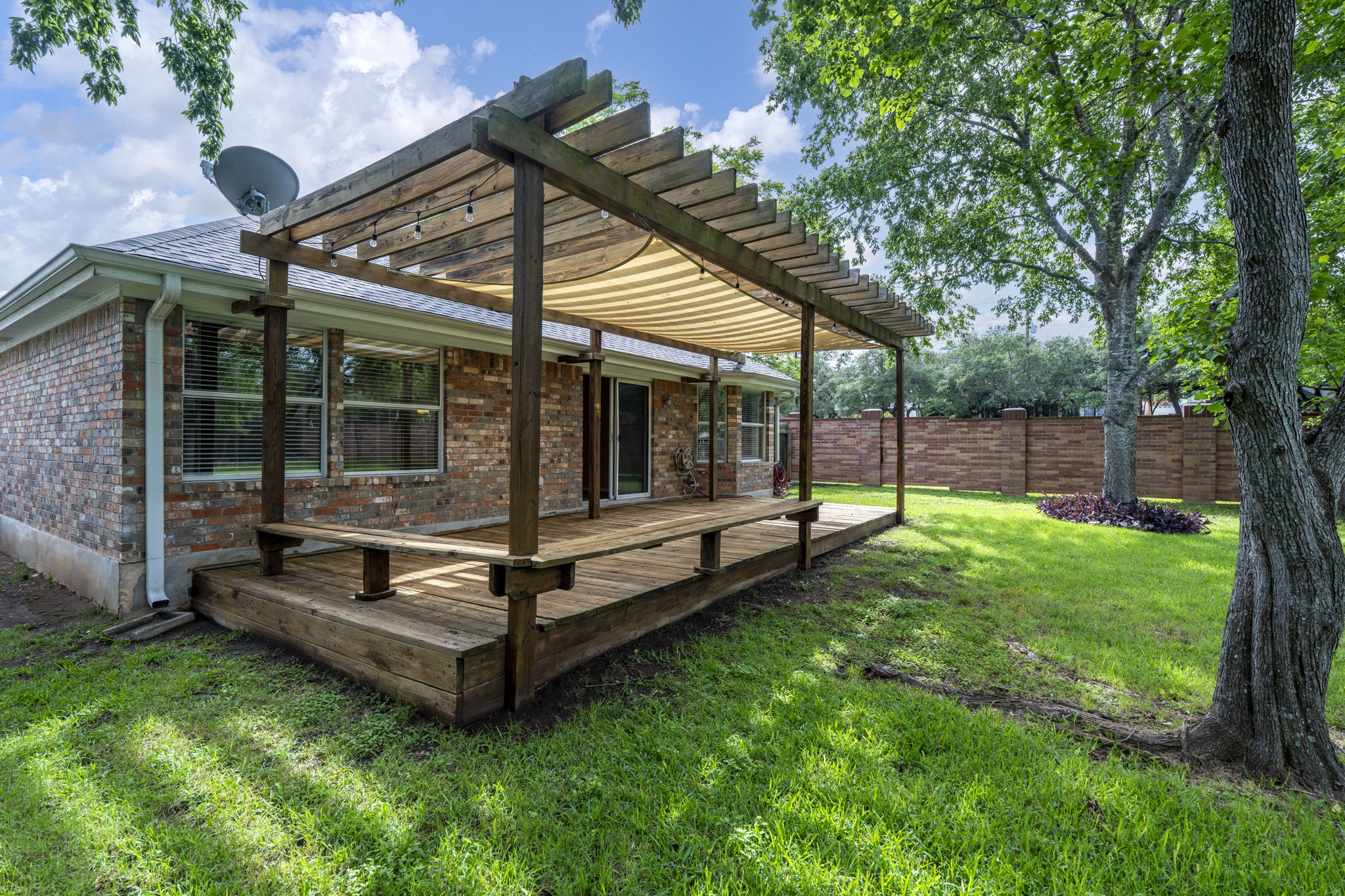 7172 Ridge Oak Road Austin, TX 78749 - Photo 13 of 40 A spacious wooden deck with a covered pergola extends from the brick-clad house into a well-maintained grassy yard.