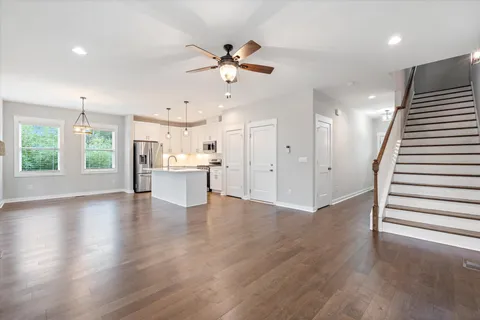 a view of an empty room with wooden floor and a kitchen