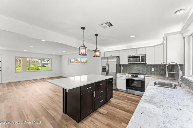 a large kitchen with stainless steel appliances granite countertop a stove a sink dishwasher and a refrigerator with wooden floor