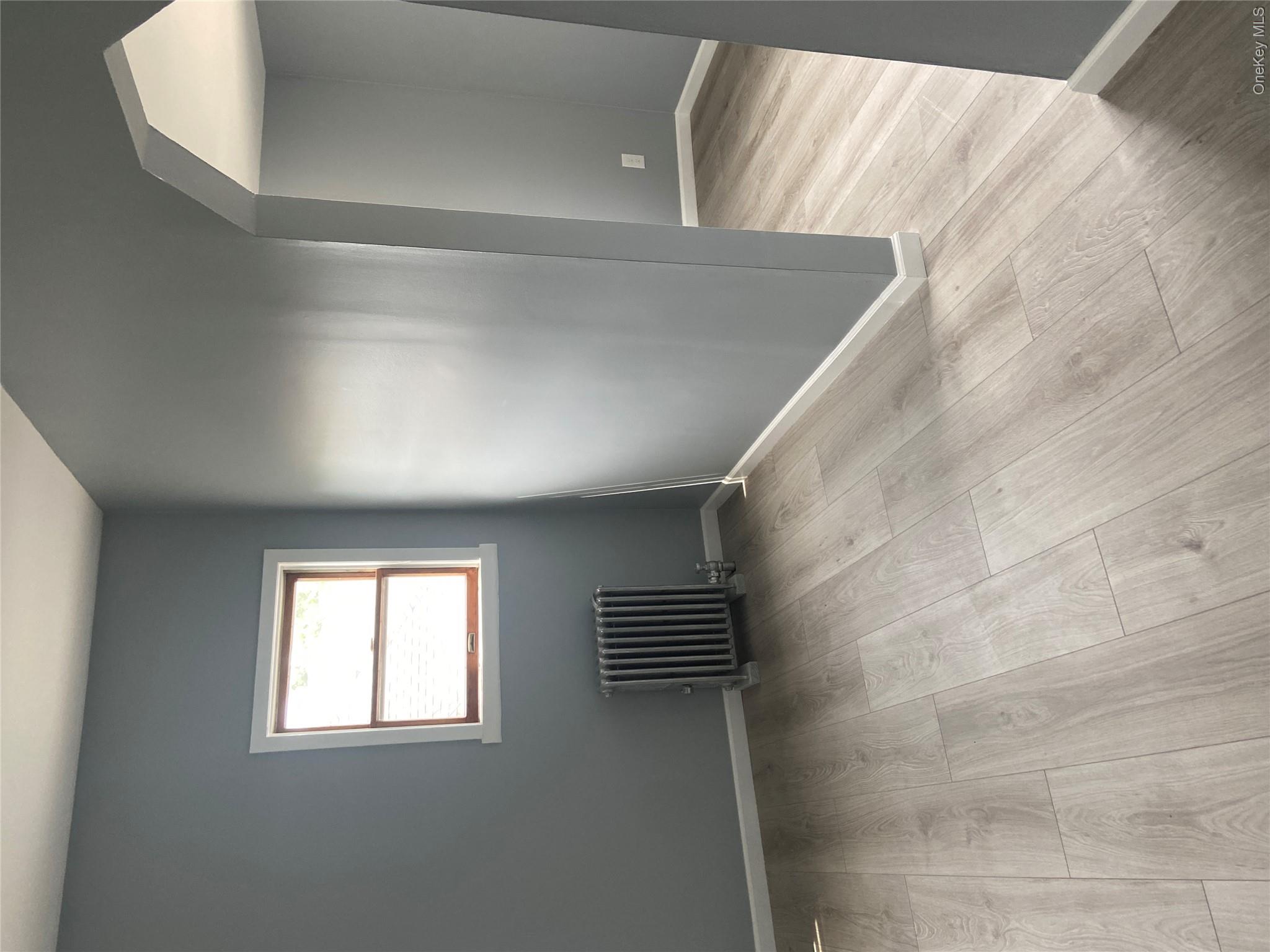 85-15 85th Street, Unit 2 Queens, NY 11421 - Photo 4 of 22 Light wood-finish flooring extends throughout the space, complemented by a radiator beneath a window with white trim