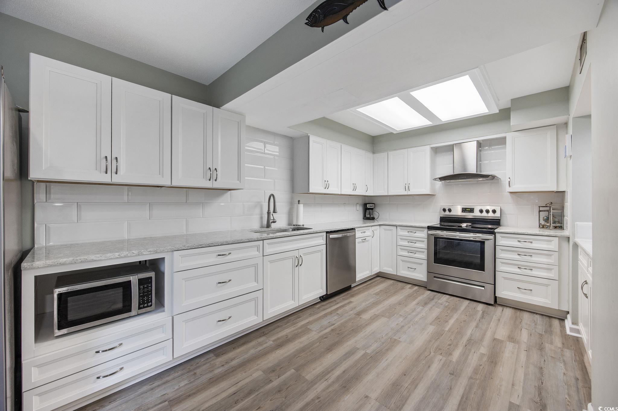 64 Bamboo Loop, Unit 161 Georgetown, SC 29440 - Photo 12 of 31 Kitchen with stainless steel appliances, wall chimney exhaust hood, a sink, light wood-type flooring, and backsplash