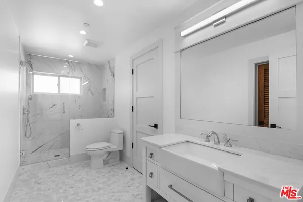 a bathroom with a toilet a sink a mirror a shower a vanity and window