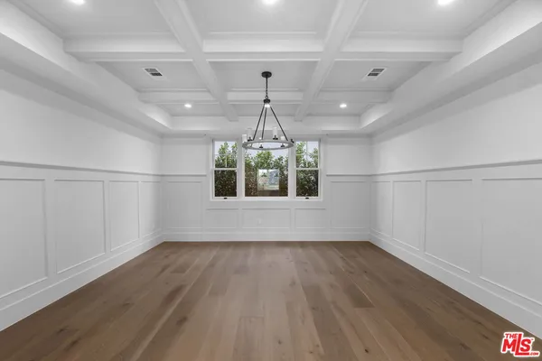 an empty room with wooden floor chandelier and windows