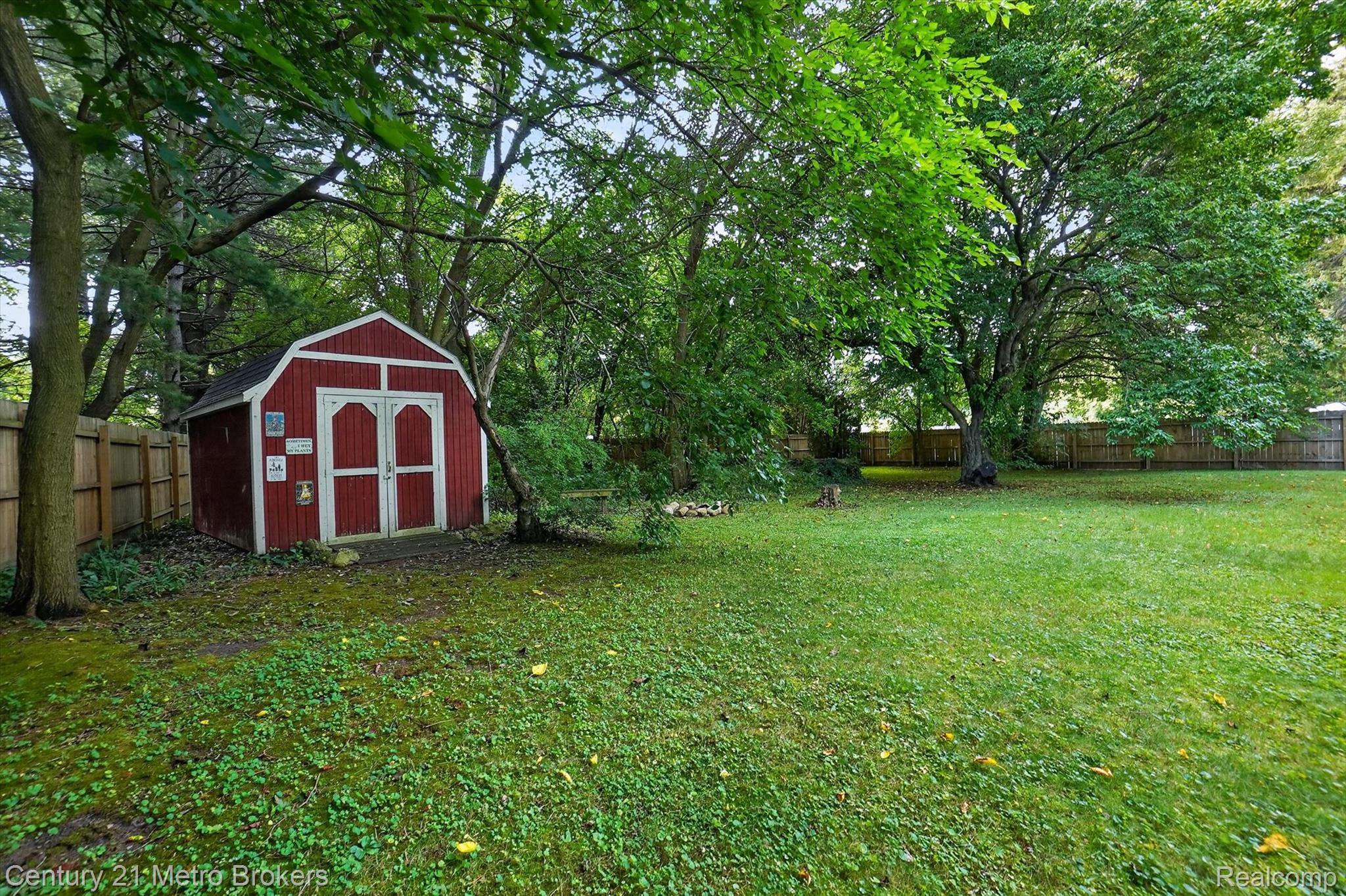 4575 Brockway Road Saginaw, MI 48638 - Photo 43 of 44 Expansive backyard featuring mature trees, a manicured lawn, wood fencing, and a red storage shed with double doors