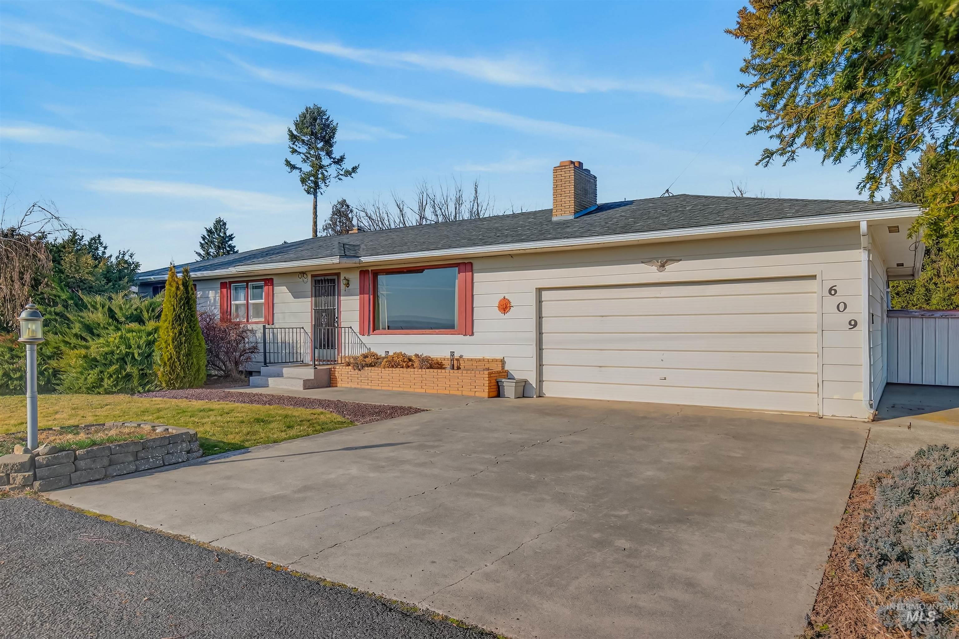 Ranch-style home with a chimney, concrete driveway, a shingled roof, and an attached garage