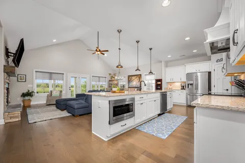 a large kitchen with stainless steel appliances granite countertop a sink a stove and a wooden floor