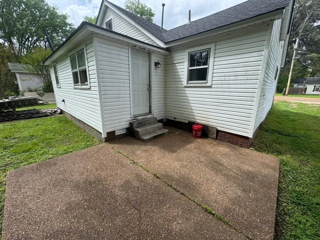 a small white house with a small yard and a large parking space