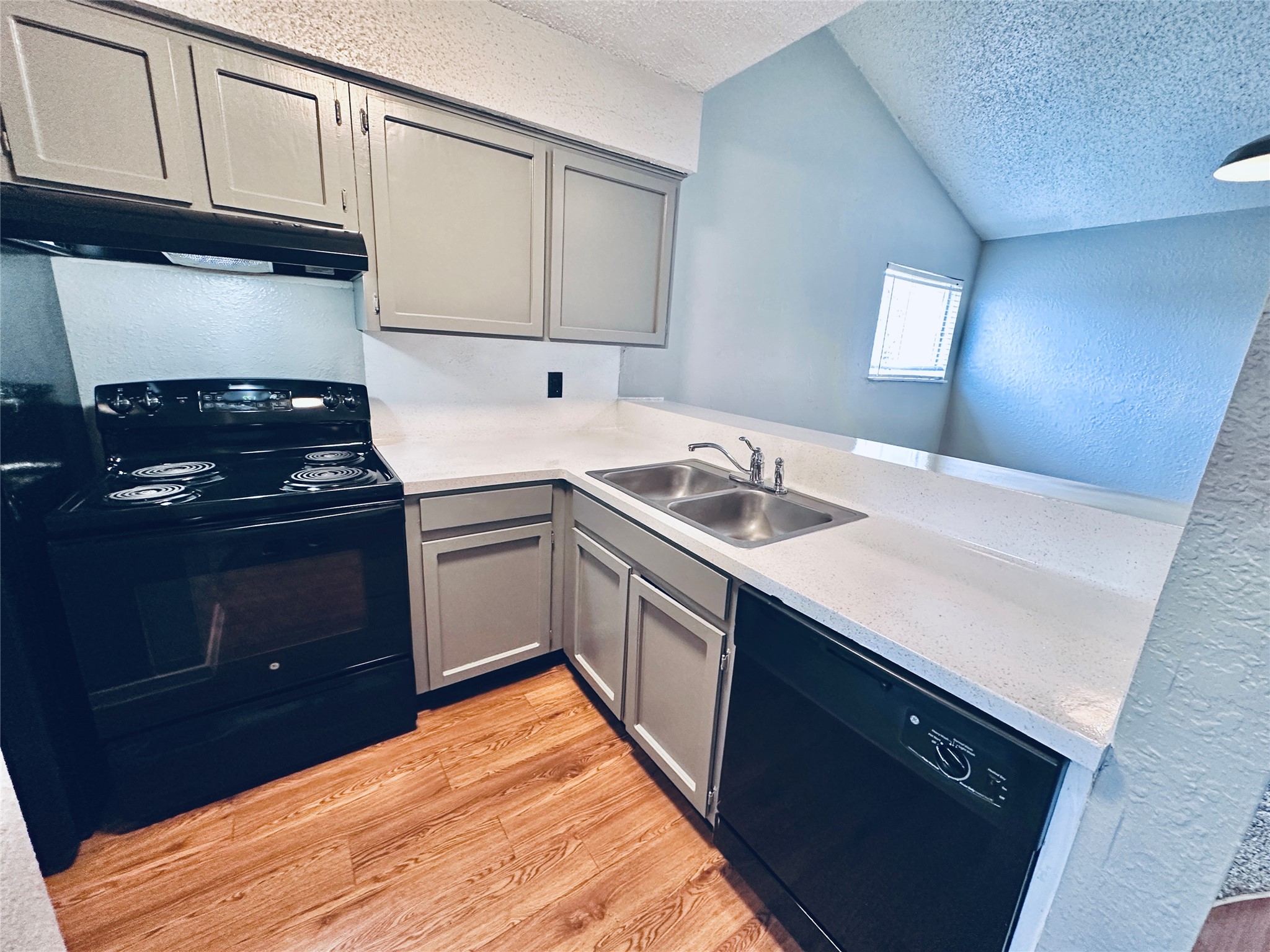 3702 South 2nd Street, Unit 321 Austin, TX 78704 - Photo 7 of 13 Kitchen featuring a textured wall, gray cabinets, black appliances, light wood-style floors, and a peninsula