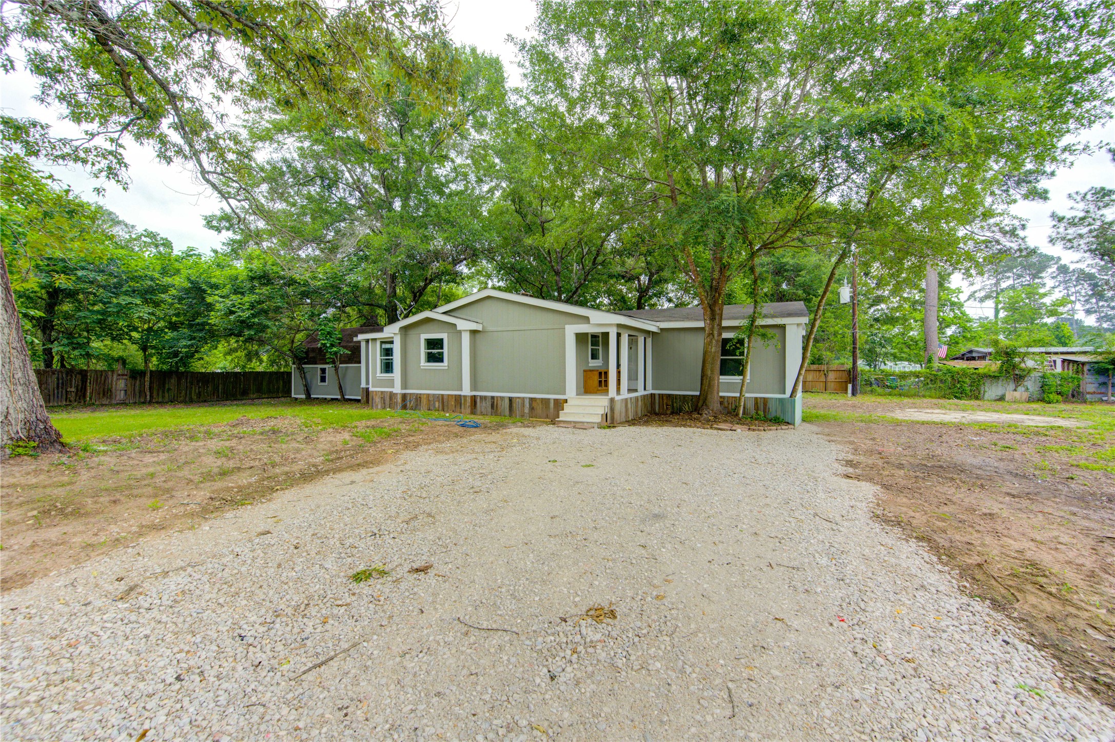 30226 Davis Street Magnolia, TX 77355 - Photo 2 of 50 Charming single-story home with a green exterior, set on a spacious lot with mature trees. Features a gravel driveway, a front porch, and a fenced backyard, offering privacy and ample outdoor space.