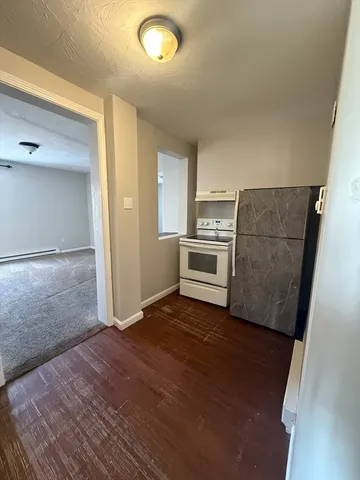 an empty room with wooden floor and kitchen