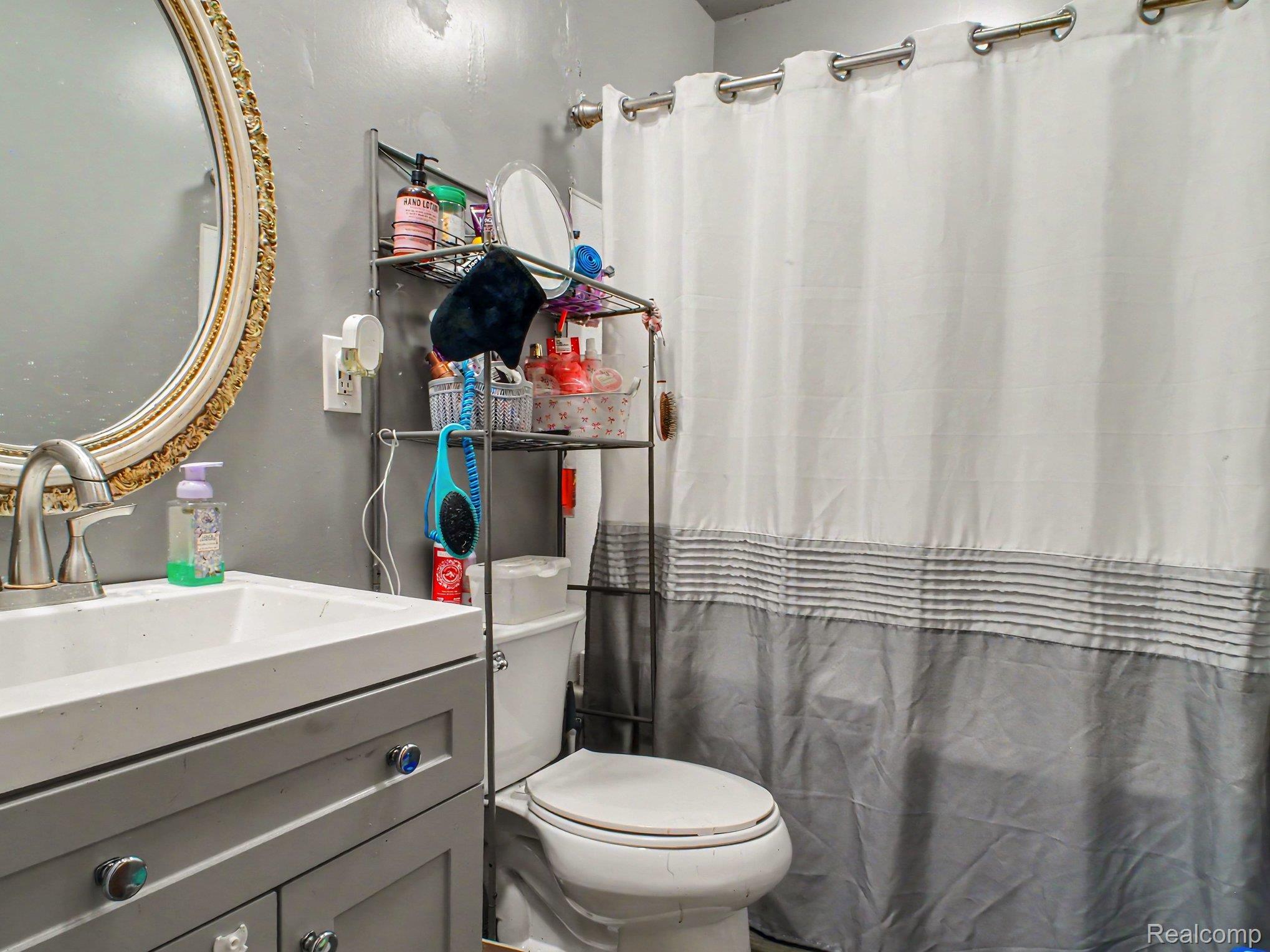 5082 North Center Road Flint, MI 48506 - Photo 16 of 21 Contemporary bathroom featuring a gray vanity with white countertop and integrated sink, polished brass-framed mirror, chrome hardware, and enclosed shower-tub combination with gray and white striped shower curtain