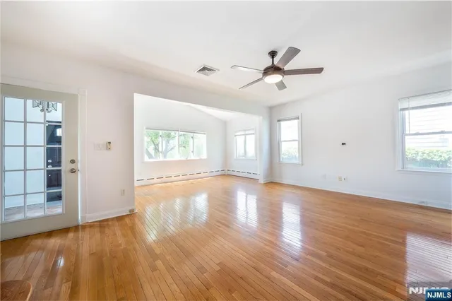an empty room with wooden floor fan and windows