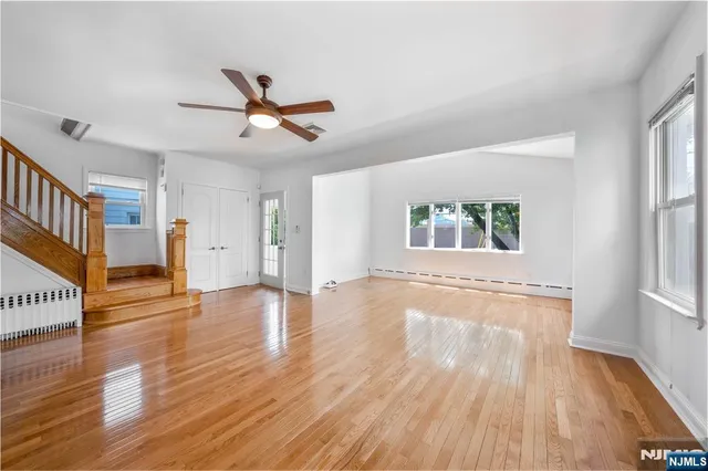 an empty room with wooden floor ceiling fan and windows