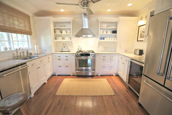 a large kitchen with a stove top oven a sink dishwasher a refrigerator and white cabinets with wooden floor